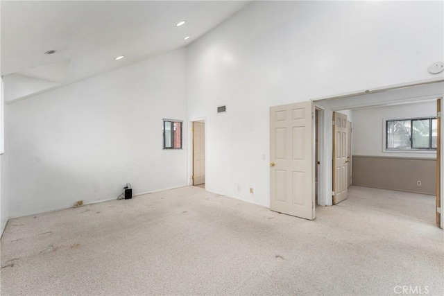 carpeted empty room with high vaulted ceiling and recessed lighting