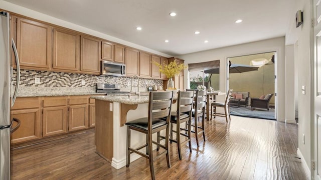 kitchen featuring tasteful backsplash, appliances with stainless steel finishes, a center island with sink, and dark wood-style flooring