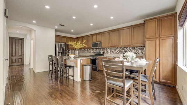 kitchen with arched walkways, stainless steel appliances, and dark wood-style flooring