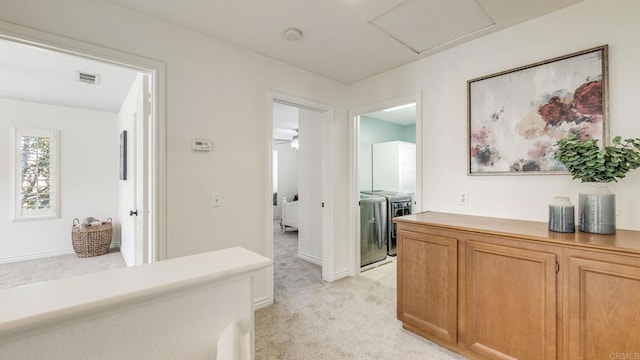 corridor featuring visible vents, light colored carpet, attic access, and independent washer and dryer