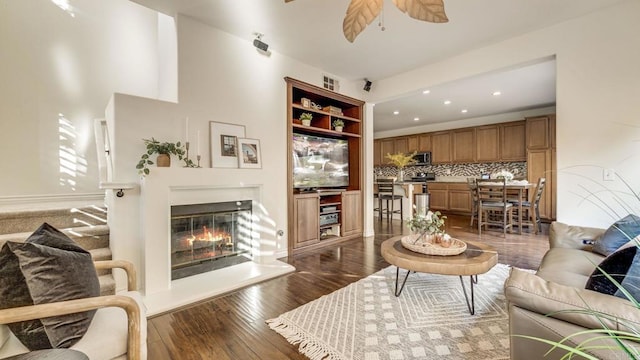 living area featuring visible vents, a ceiling fan, a glass covered fireplace, and dark wood-style flooring