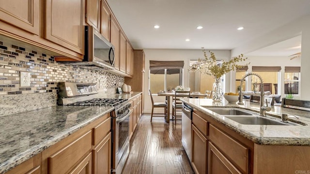 kitchen with brown cabinetry, dark wood-style flooring, a sink, appliances with stainless steel finishes, and backsplash