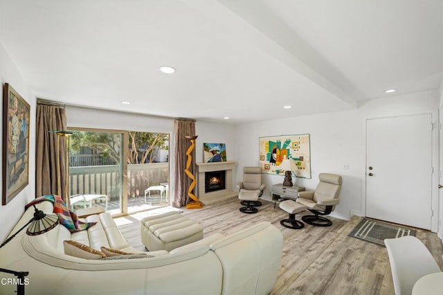 living area with a warm lit fireplace, baseboards, wood finished floors, and recessed lighting