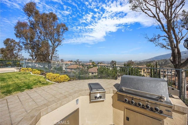 view of patio / terrace with exterior kitchen, a grill, fence, and a mountain view