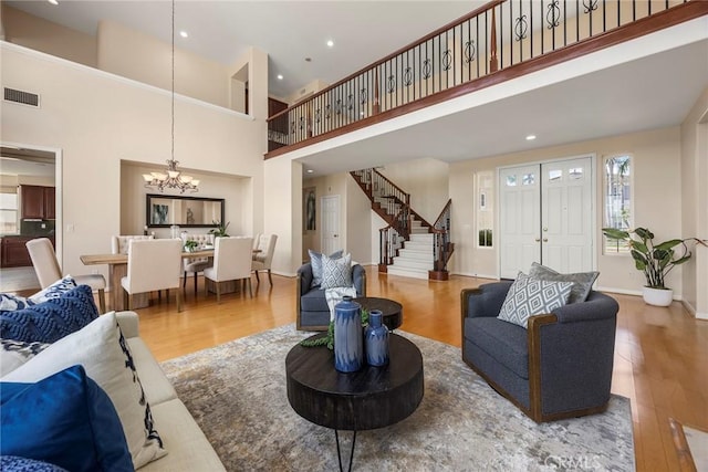 living room with a chandelier, wood finished floors, visible vents, baseboards, and stairs