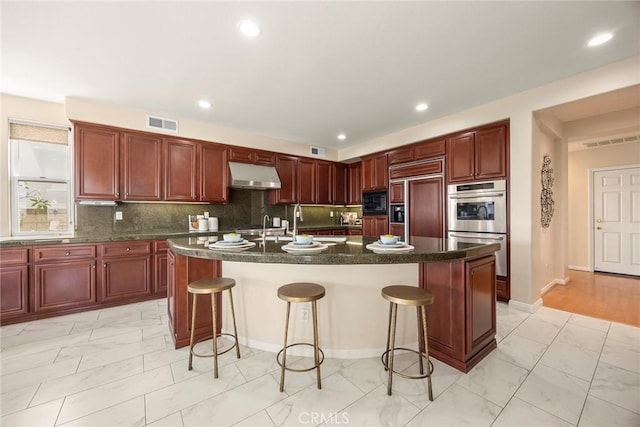 kitchen featuring built in appliances, under cabinet range hood, visible vents, dark brown cabinets, and marble finish floor