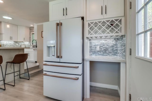 kitchen featuring light countertops, white refrigerator with ice dispenser, white cabinetry, and decorative backsplash