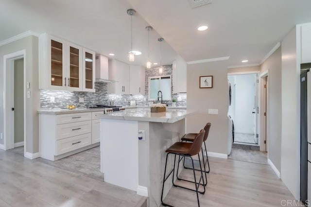 kitchen with a center island, a breakfast bar area, decorative backsplash, glass insert cabinets, and wall chimney exhaust hood