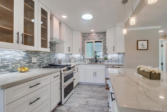 kitchen with light stone counters, decorative backsplash, a sink, wall chimney range hood, and double oven range