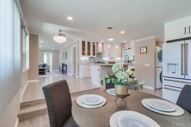 dining space featuring ornamental molding, light wood-type flooring, stacked washer and clothes dryer, and visible vents