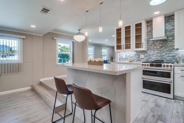 kitchen featuring visible vents, range with two ovens, decorative backsplash, wall chimney range hood, and a kitchen bar