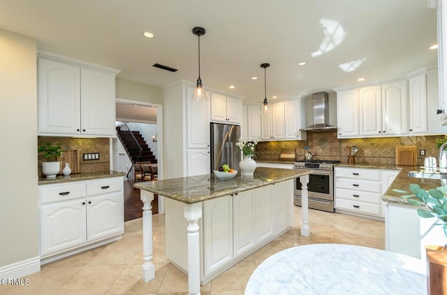 kitchen featuring dark stone counters, a sink, appliances with stainless steel finishes, white cabinetry, and wall chimney range hood