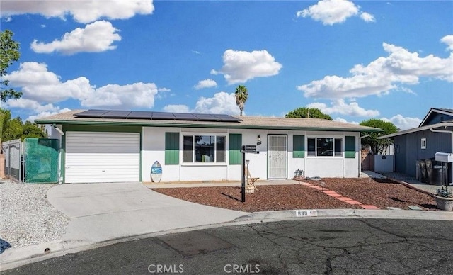 ranch-style house with a gate, driveway, solar panels, an attached garage, and stucco siding