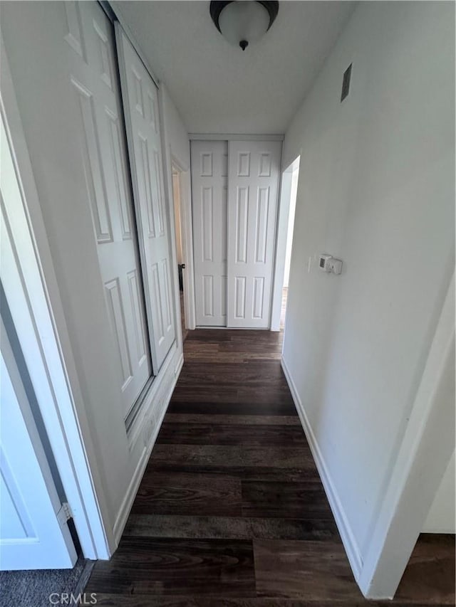 hall with visible vents, baseboards, and dark wood-style flooring