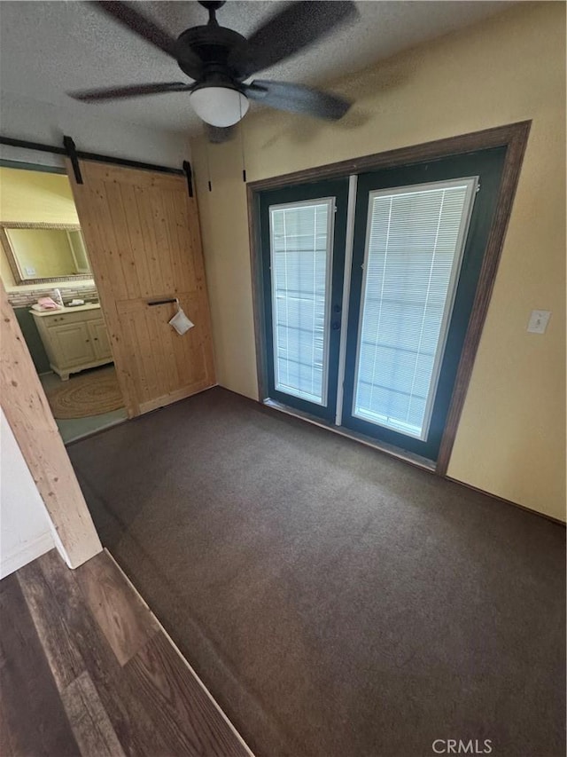 empty room with a textured ceiling, dark wood finished floors, dark carpet, a barn door, and ceiling fan
