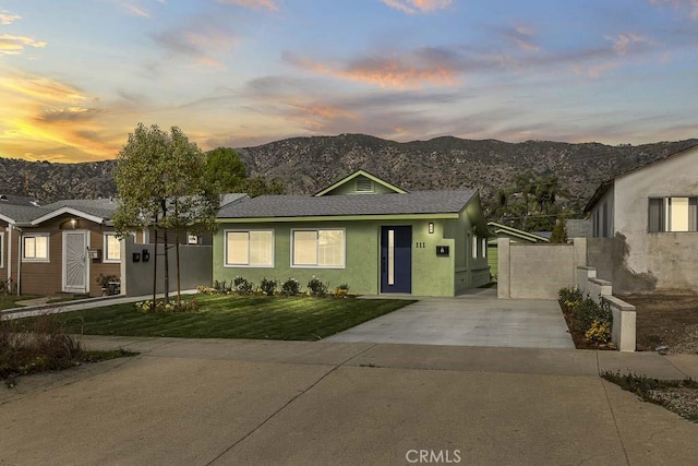 view of front of property featuring a lawn, concrete driveway, fence, a mountain view, and stucco siding