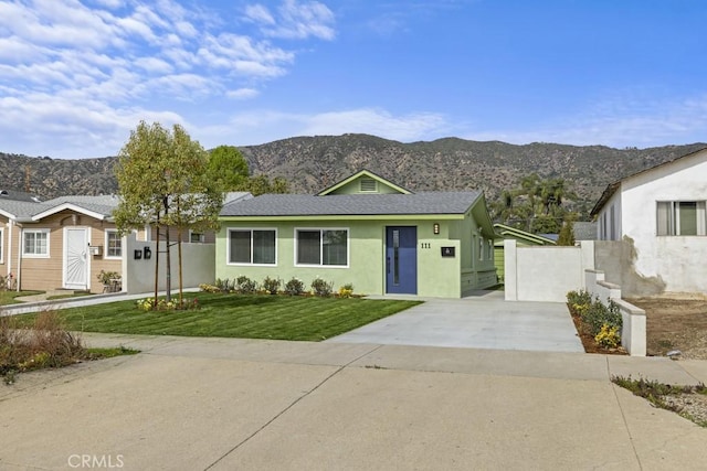 view of front facade featuring a mountain view, fence, driveway, stucco siding, and a front yard