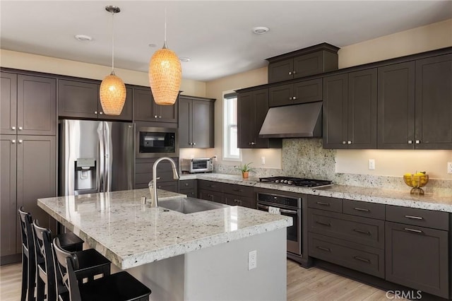 kitchen with stainless steel appliances, a sink, light wood-type flooring, a kitchen bar, and exhaust hood