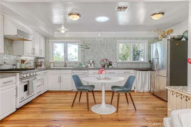 kitchen featuring range with gas cooktop, stainless steel refrigerator with ice dispenser, light wood finished floors, a wealth of natural light, and visible vents