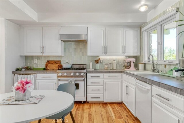 kitchen with light wood finished floors, high end stainless steel range oven, a sink, white dishwasher, and wall chimney exhaust hood