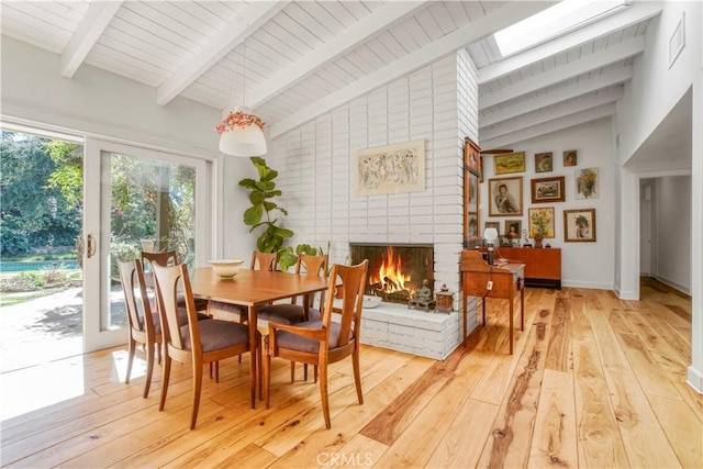 dining room featuring a brick fireplace, vaulted ceiling with skylight, and light wood finished floors