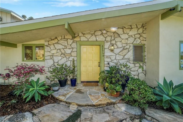 view of exterior entry featuring stone siding and stucco siding