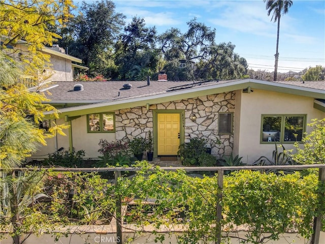 mid-century home featuring stone siding, roof with shingles, a chimney, and stucco siding