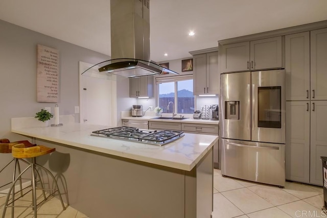 kitchen featuring island range hood, a breakfast bar area, a peninsula, stainless steel appliances, and a sink