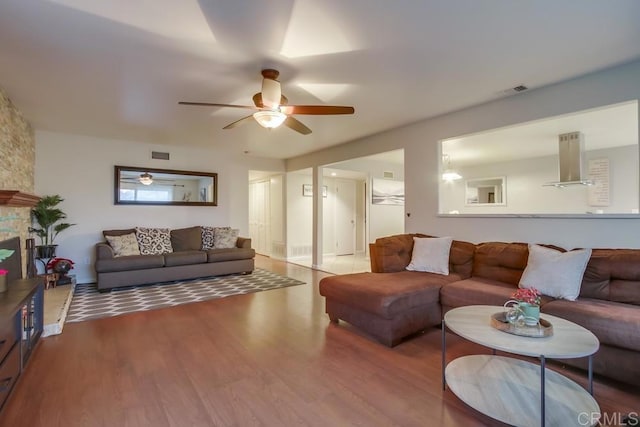 living room with ceiling fan, a fireplace, wood finished floors, and visible vents