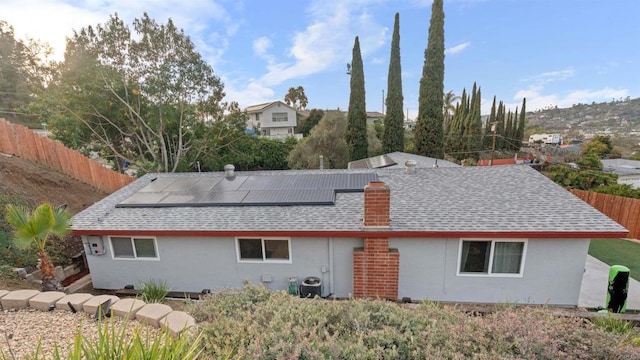 back of property featuring central AC unit, solar panels, roof with shingles, fence, and stucco siding