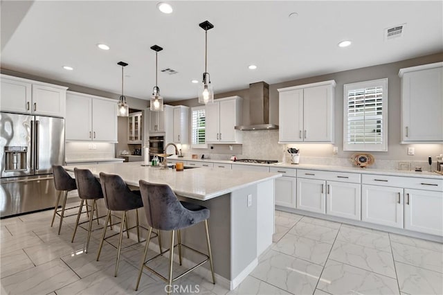 kitchen with marble finish floor, a breakfast bar area, appliances with stainless steel finishes, a sink, and wall chimney exhaust hood