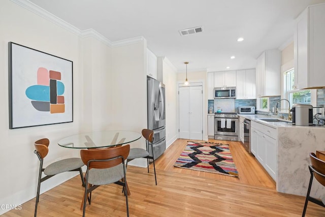 kitchen featuring visible vents, crown molding, stainless steel appliances, white cabinetry, and a sink