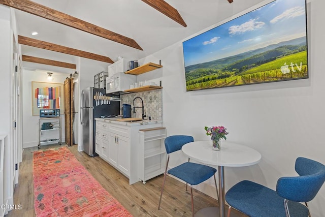 kitchen featuring beam ceiling, light wood finished floors, open shelves, white cabinets, and light countertops