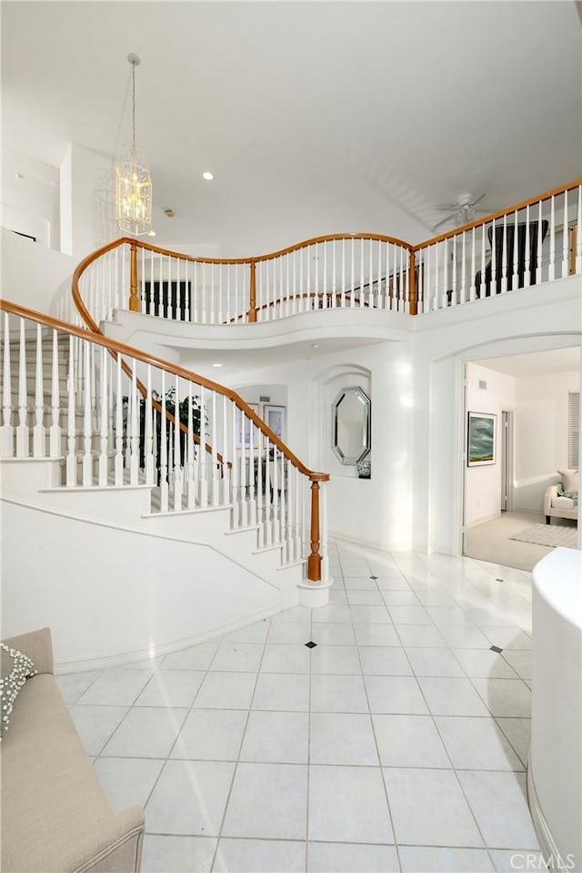 stairs with a towering ceiling, recessed lighting, ceiling fan with notable chandelier, and tile patterned floors