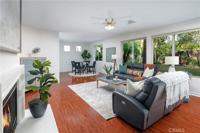 living room featuring ceiling fan, wood finished floors, visible vents, baseboards, and a glass covered fireplace