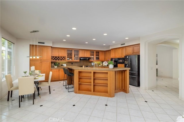 kitchen featuring brown cabinetry, arched walkways, under cabinet range hood, and black appliances