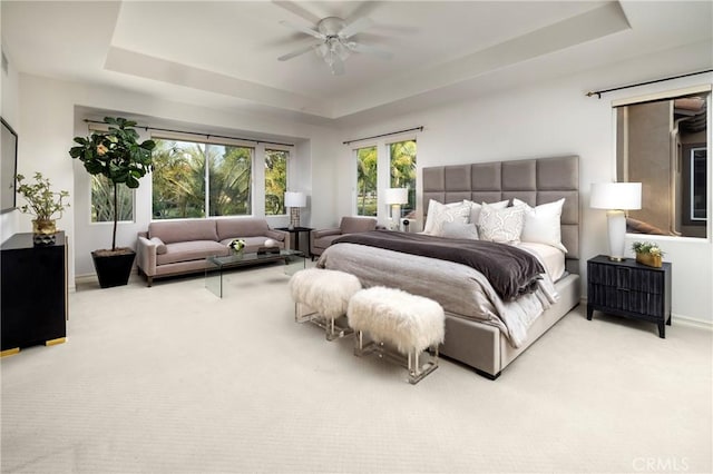 carpeted bedroom featuring baseboards, a tray ceiling, and a ceiling fan