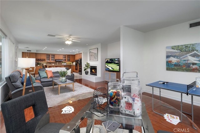 living room featuring visible vents, dark wood finished floors, a lit fireplace, and baseboards