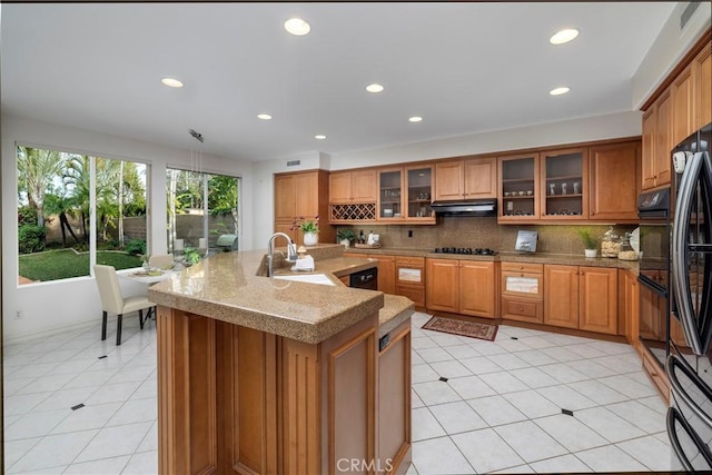 kitchen featuring under cabinet range hood, brown cabinetry, and a sink