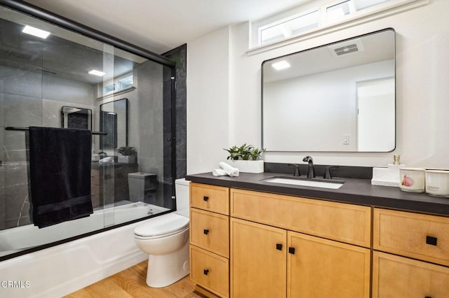 full bath with visible vents, toilet, wood finished floors, shower / bath combination with glass door, and vanity