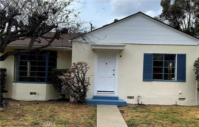 bungalow-style home with stucco siding, a front lawn, and crawl space