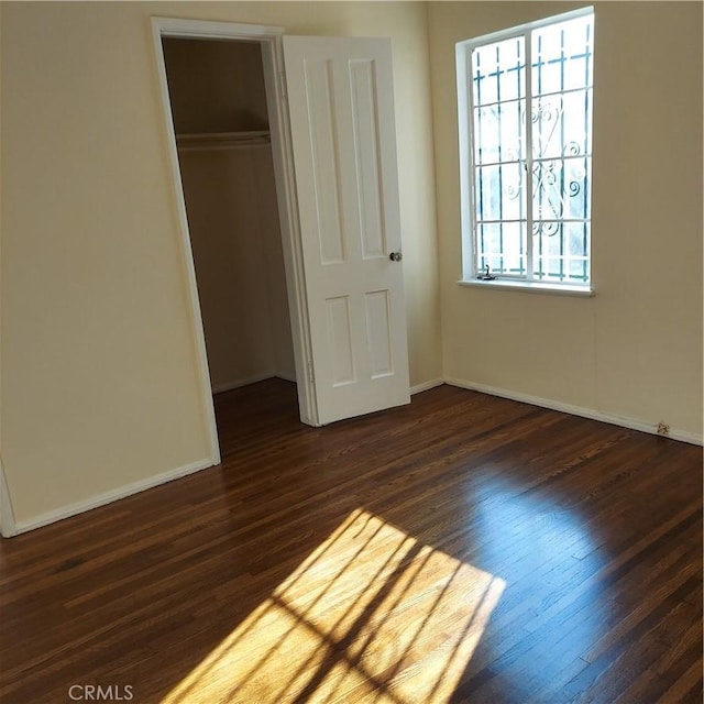 unfurnished bedroom featuring a closet, baseboards, and dark wood finished floors