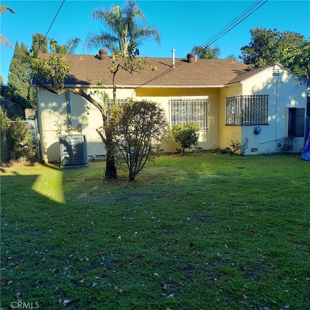 rear view of house with stucco siding, a yard, and cooling unit