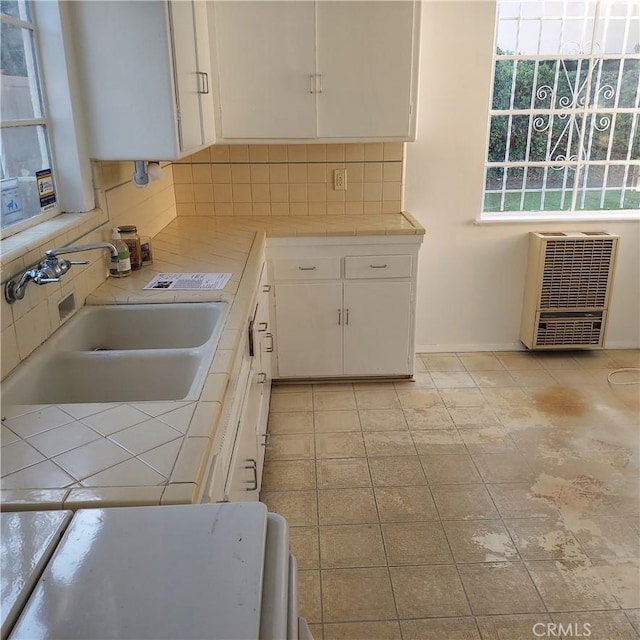 kitchen featuring tasteful backsplash, tile counters, heating unit, white cabinetry, and a sink