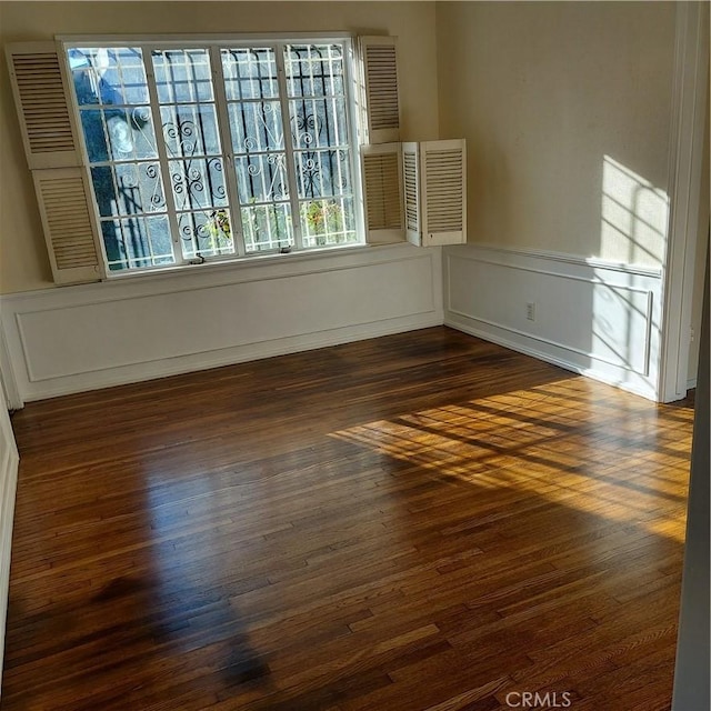 empty room with wainscoting, dark wood-style flooring, and a decorative wall