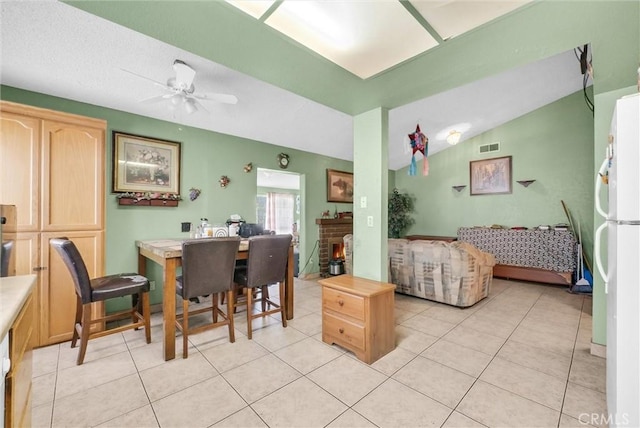 dining room with a ceiling fan, light tile patterned flooring, vaulted ceiling, and a fireplace