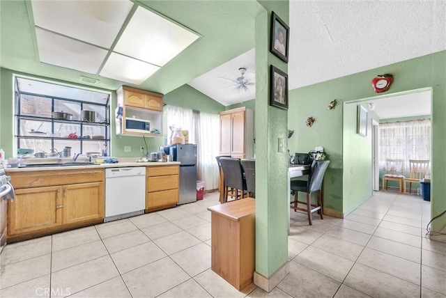 kitchen featuring dishwasher, freestanding refrigerator, light countertops, vaulted ceiling, and light tile patterned flooring