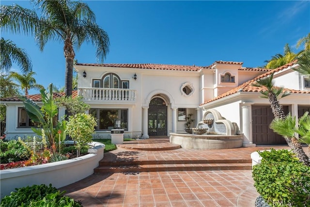 rear view of house with french doors, a tile roof, a balcony, and stucco siding