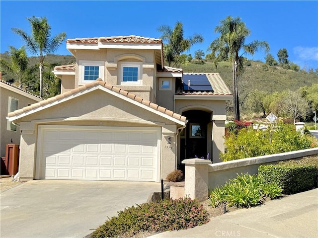 mediterranean / spanish home featuring stucco siding, solar panels, concrete driveway, and a tiled roof