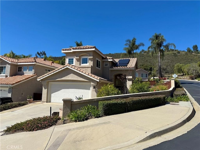 mediterranean / spanish-style house with solar panels, stucco siding, concrete driveway, a garage, and a fenced front yard